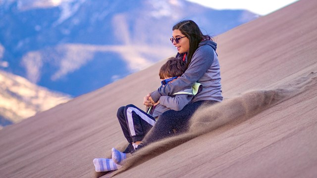 Teen girl and boy sliding down a dune on a sand sled