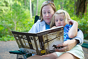 A mother and child sit in a camp chair reading a Jr. Ranger booklet