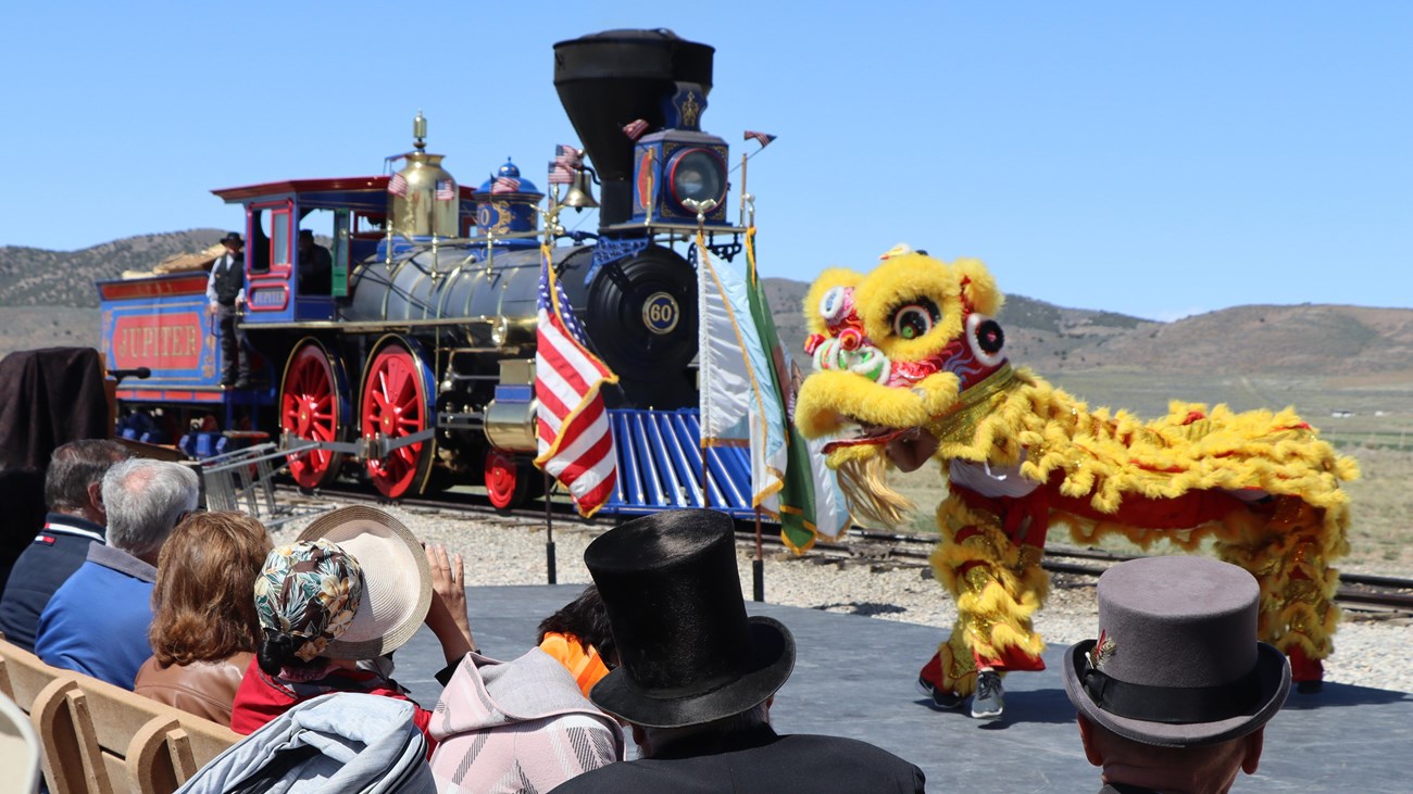 Crowd watching dancers wearing a traditional Chinese dragon outfit in front of a historic train