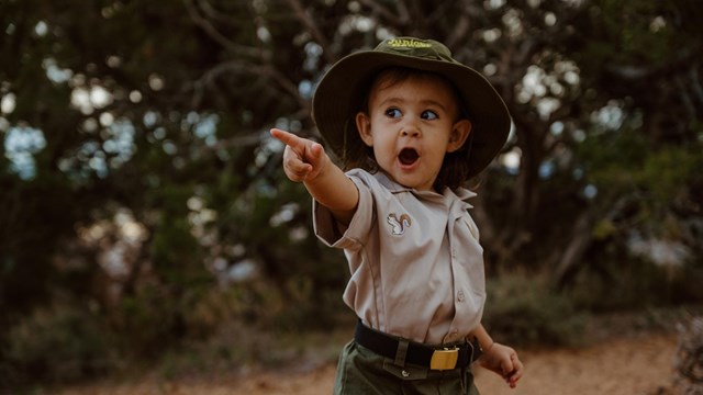 Toddler in Junior Ranger outfit pointing with an expression of amazement.