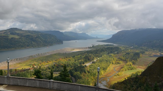 Columbia River runs through dark green hill sides illuminated by a ray of light on a cloudy day.