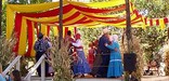 Couples in period clothing dance on a stage with overhanging banners