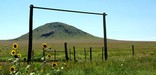 A large round mound is framed by a wood entry gate with sunflowers on the Santa Fe Trail