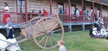 An oxcart rests in short grass while colorfully dressed reinactors enjoy Rendezvous Days on the front porch of the Great Hall.
