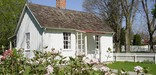 A small white cottage with blossoming pink flowers in front.