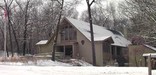 a high peaked roof building surrounded by large trees and a light snow on the ground