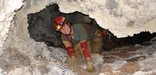 A caver crawls under a frostwork rim (NPS Photo)