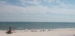 View of uncrowded mid-week lifeguarded beach, with calm waves and puffy clouds in clear blue sky.