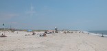 View looking down uncrowded mid-week lifeguarded beach, with swimmers in the breaking surf and high dunes in the distance.