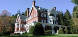 Three story brick mansion with wide porch, white trim, tall chimneys, shrubs and green lawn. Photo by Jack Boucher.