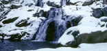 Icy water cascades from snow-covered rocks in this winter waterfall picture.