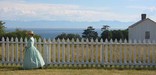 A re-enactor strolls along the parade ground fence at American Camp with the Laundress Quarters in the background.