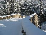 Woman skis over historic stone bridge.