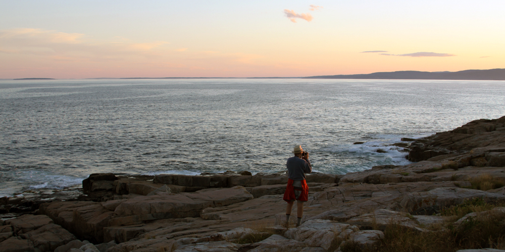 A visitor photographs the sunset along the Schoodic Peninsula shoreline.