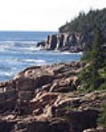 The ocean meets granite cliffs topped by evergreens.