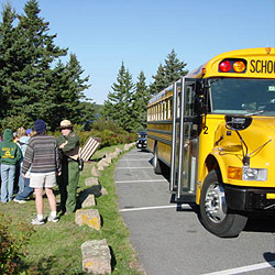 A park ranger stands with a teacher and students near a bus.
