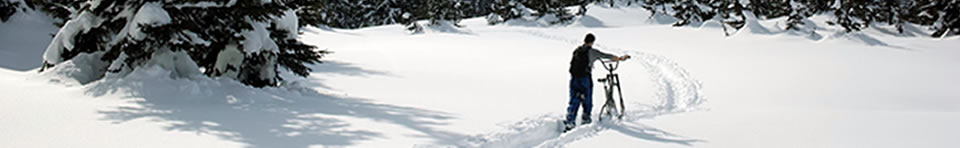Winter biker pushing through snow on mountainous trail.