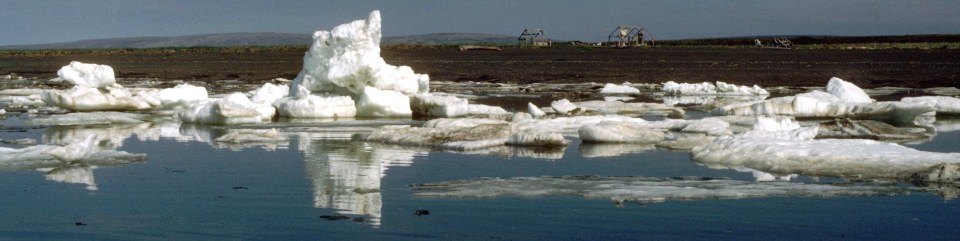 Chunks of melting sea ice along a shoreline and subsistence camps on the beach in the background.