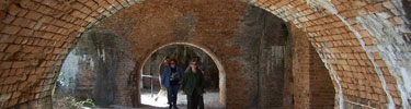 Three visitors walk under tan brick arches that are features of Fort Pickens.