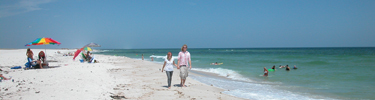Visitors walking on the white sandy beach with blue water in background.