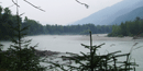 Taiya River with calm waters snaking through misty fog with blue mountain backdrop Taiya River with calm waters snaking through misty fog with blue mountain backdrop