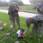 Men in uniforms and a little boy put flags on national cemetery graves