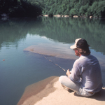 Man seated on rock and fishing in river