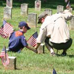 A cub scout and his father place flags at grave sites in Stones River National Cemetery.