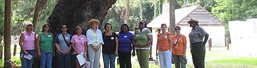 Teachers standing under an oak tree with slave quarters in background.