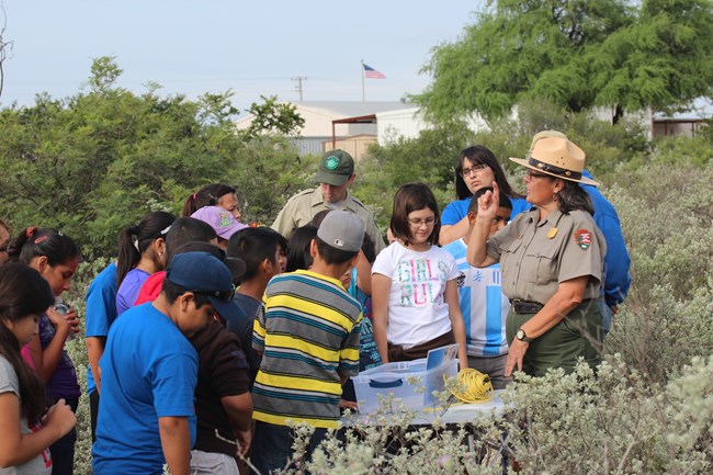 Park Ranger providing instruction on a trail with middle school students crowded around, standing, and listening intently.