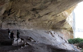 Several people inside a large cave standing near an interpretive sign.