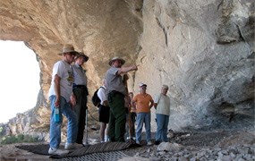 A uniformed guide explaining off-camera objects to four people inside a cave.