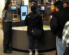 Park Ranger talking with visitors about the vastness of Alaska's public lands using a three-dimensional touchable map.