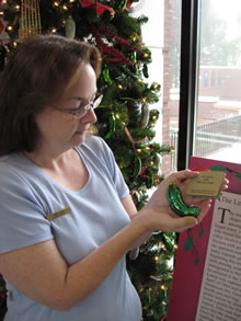 Woman holding a glass pickle ornament by a Christmas Tree.