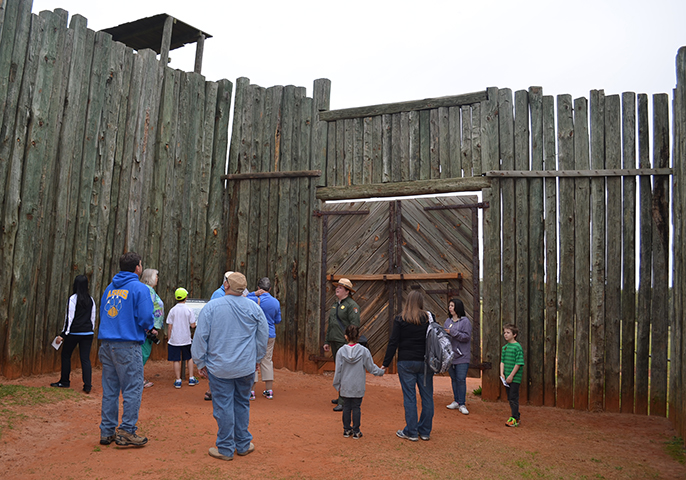 Park ranger and visitors stand inside wooden stockade gate