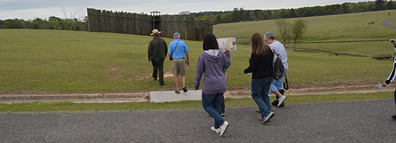 Park ranger leads a group of visitors toward a tall wooden structure with an open gate.