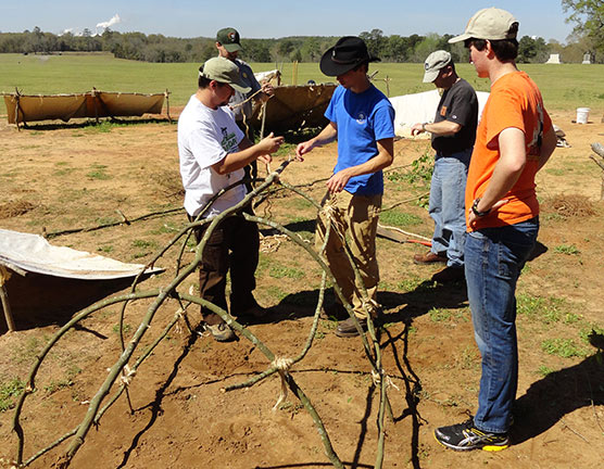 Staff and volunteers construct a shelter with branches.