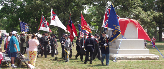 Civil War soldiers carry flags of the north and south past a stone monument
