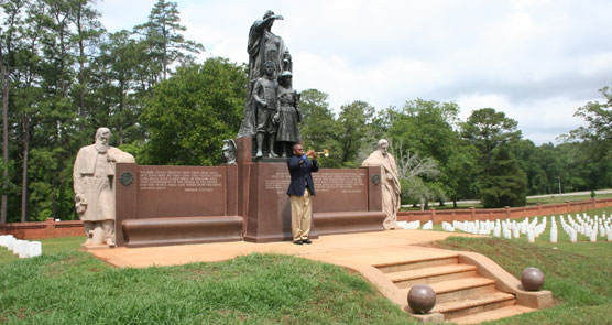 Young man blowing Taps on a bugle below a bronze and stone statue