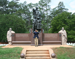 Bugler blowing taps below a bronze and stone monument