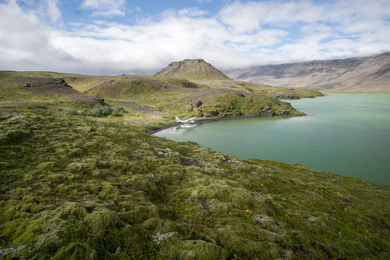 Aniakchak Crater tundra hummocks over a rolling volcanic landscape as a float plan sits on a lake in the middle distance