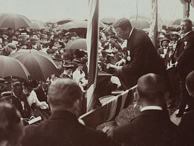 Roosevelt standing on elevated platform, delivering speech to a crowd