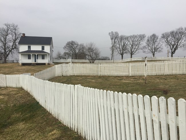 fog shrouds a white farmhouse with white picket fence