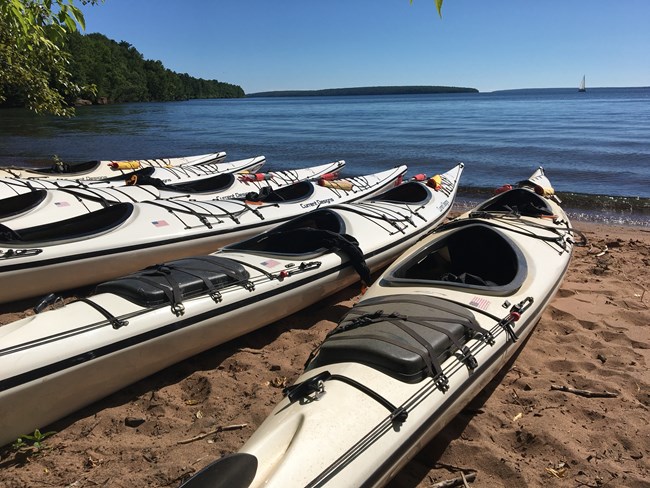 6 Tandem White Sea Kayaks sitting on beach at water's edge with islands in the background.