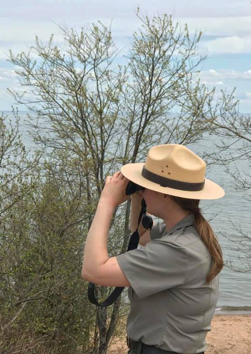 A park ranger looks across a lake with binoculars.