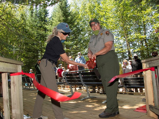A woman in a Friends hat and a woman in a park ranger uniform cut through a ribbon with a giant pair of scissors.