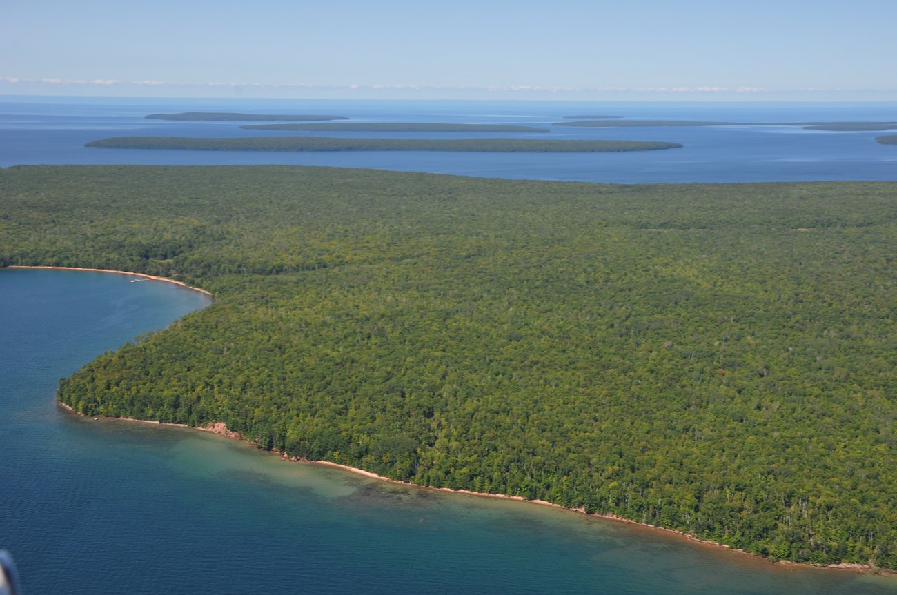 Aerial view of green forest covered islands surrounded by blue water.