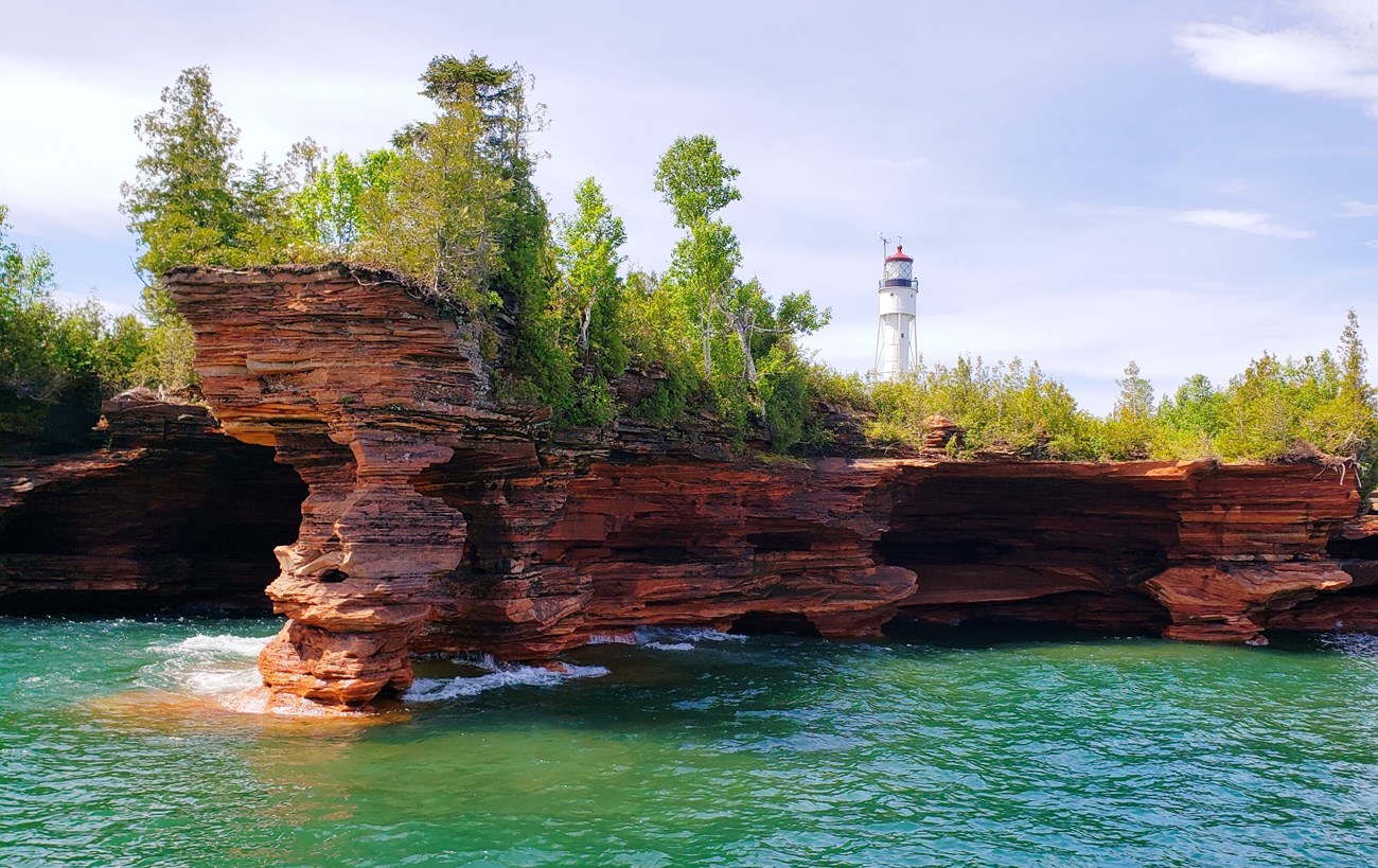 Reddish sandstone cliffs and caves with a distant lighthouse tower.