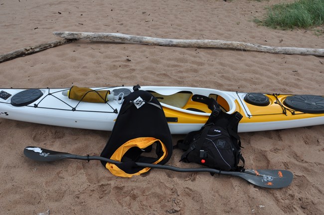White and yellow kayak with life jacket, paddle, spray skirt, and bilge pump.
