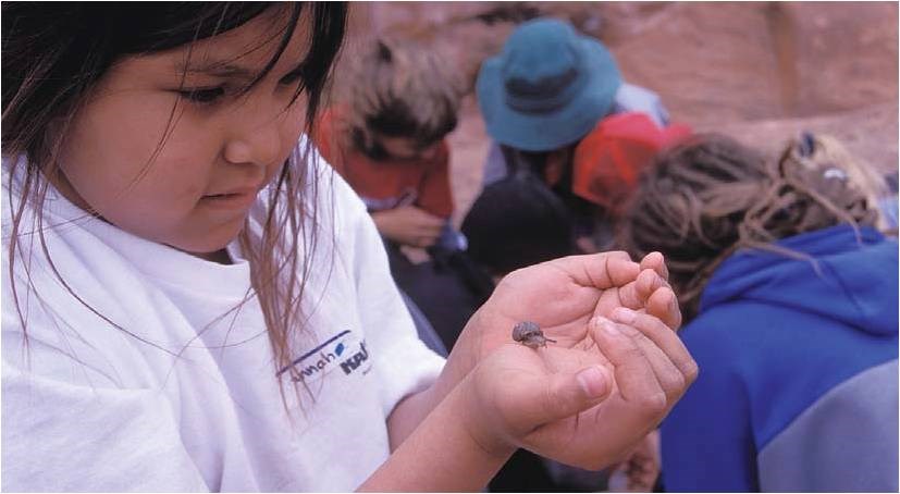A young girl holding and looking at a small snail.